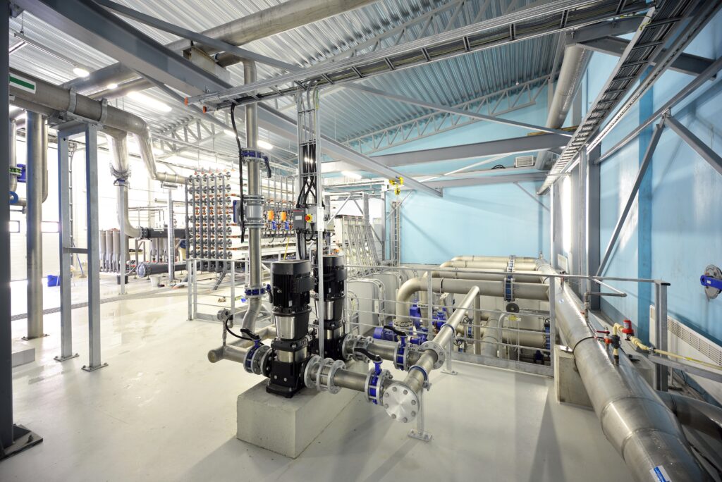 Mechanical plant room with large pipework, valves, and pumps in an industrial building